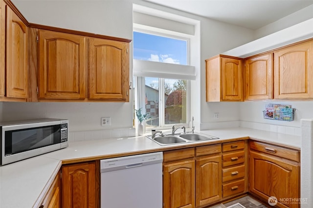 kitchen with brown cabinetry, dishwasher, a sink, light countertops, and stainless steel microwave