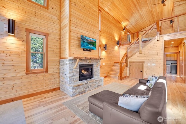 living area with wood finished floors, a stone fireplace, wooden walls, high vaulted ceiling, and stairway