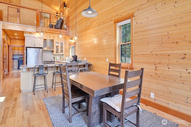 dining space featuring wooden walls, high vaulted ceiling, light wood finished floors, and wooden ceiling