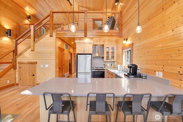 kitchen with wall chimney range hood, fridge, stove, high vaulted ceiling, and wooden walls