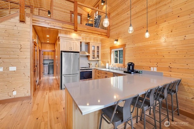 kitchen featuring a peninsula, appliances with stainless steel finishes, wood walls, and wall chimney exhaust hood