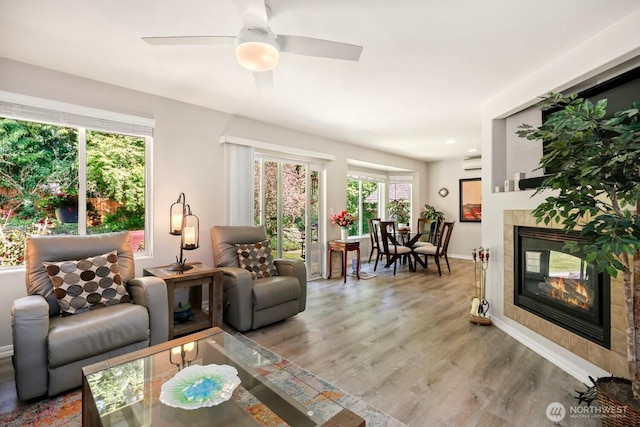 living area with a tile fireplace, light wood-style flooring, baseboards, and a ceiling fan