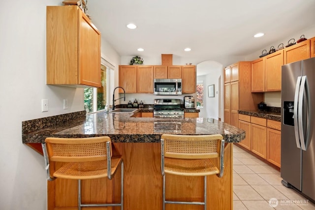 kitchen with appliances with stainless steel finishes, a sink, a peninsula, recessed lighting, and arched walkways