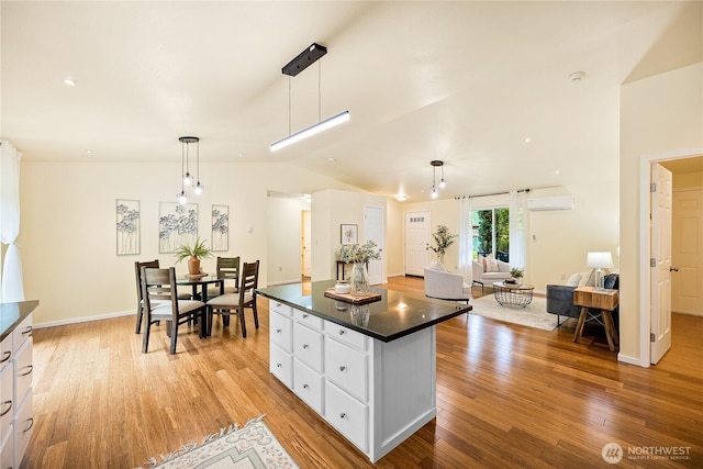 18514 71st St NW, Vaughn, WA 98394 - kitchen with dark countertops, lofted ceiling, light wood-type flooring, white cabinetry, and an AC wall unit