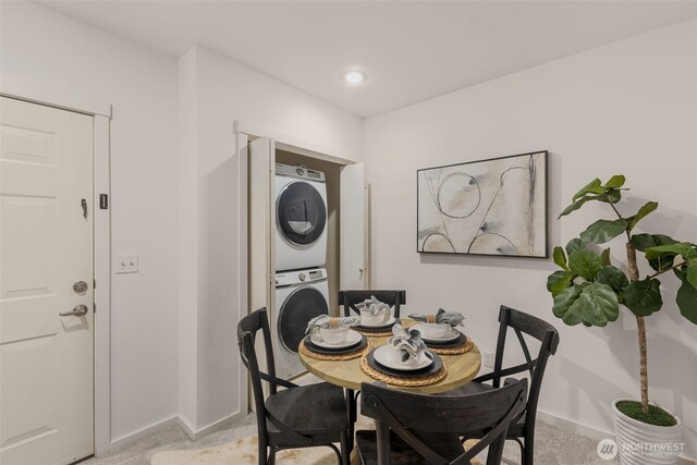 dining space featuring stacked washing maching and dryer, baseboards, and light carpet