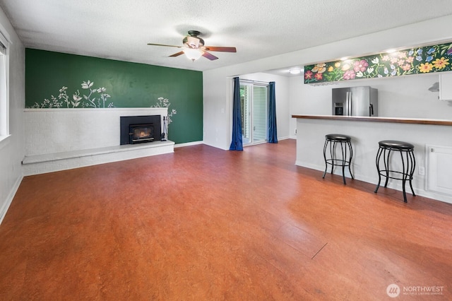 unfurnished living room with baseboards, ceiling fan, a wood stove, and a textured ceiling