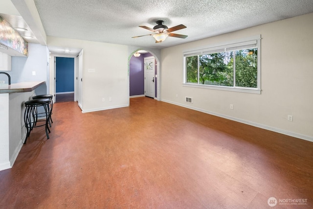 unfurnished living room featuring a textured ceiling, ceiling fan, baseboards, and arched walkways