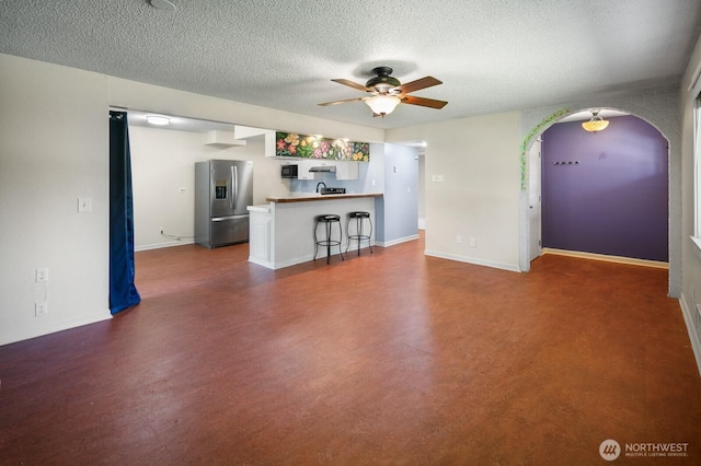 unfurnished living room featuring ceiling fan, a textured ceiling, arched walkways, a sink, and baseboards