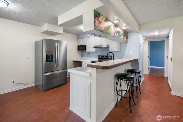 kitchen featuring a peninsula, a breakfast bar, baseboards, a textured ceiling, and appliances with stainless steel finishes