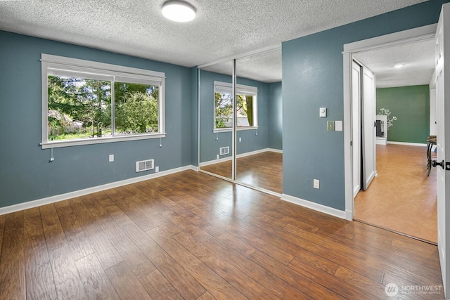 unfurnished bedroom with a textured ceiling, hardwood / wood-style floors, baseboards, visible vents, and a closet