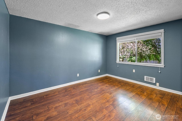 unfurnished room with baseboards, dark wood-style flooring, a textured ceiling, and visible vents