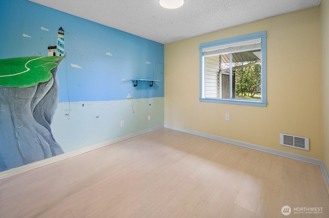 empty room with wood finished floors, baseboards, a textured ceiling, and visible vents