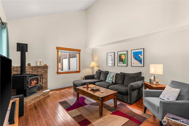 living room with hardwood / wood-style floors, baseboards, high vaulted ceiling, and a wood stove