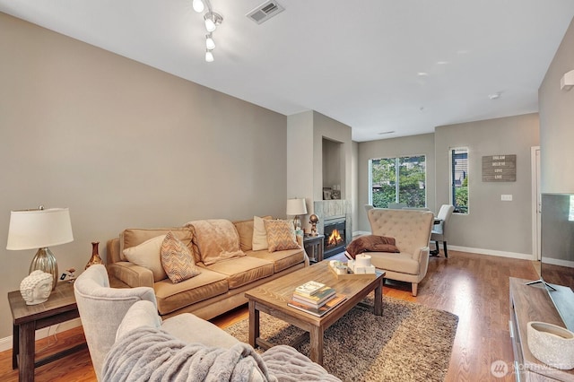 living area with a glass covered fireplace, baseboards, light wood-type flooring, and visible vents