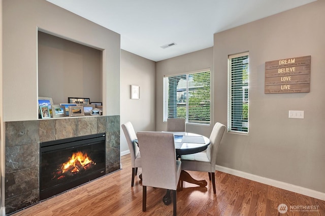dining space with baseboards, visible vents, wood finished floors, and a tile fireplace