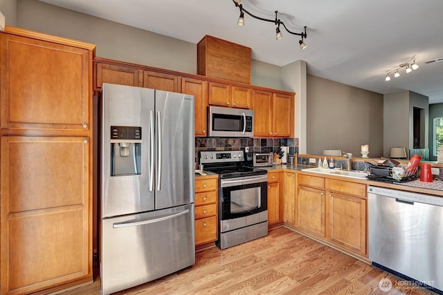 kitchen featuring appliances with stainless steel finishes, track lighting, a sink, light wood-style floors, and tasteful backsplash