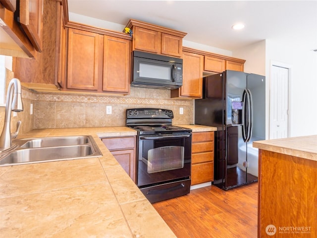 kitchen with a sink, light countertops, black appliances, and light wood-type flooring