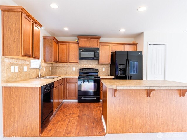 kitchen with a sink, light countertops, light wood-style flooring, a kitchen bar, and black appliances