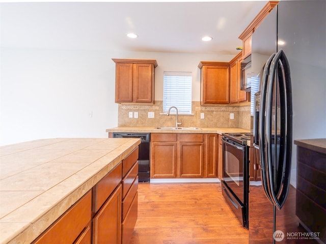 kitchen with backsplash, brown cabinets, a sink, black appliances, and light wood finished floors