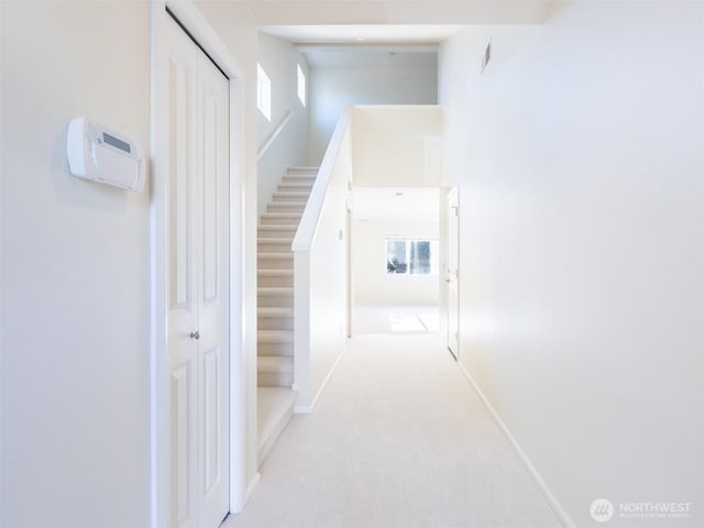 hall featuring baseboards, visible vents, and light colored carpet