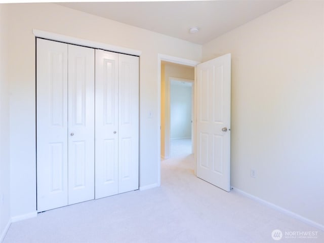 unfurnished bedroom with baseboards, light colored carpet, and a closet