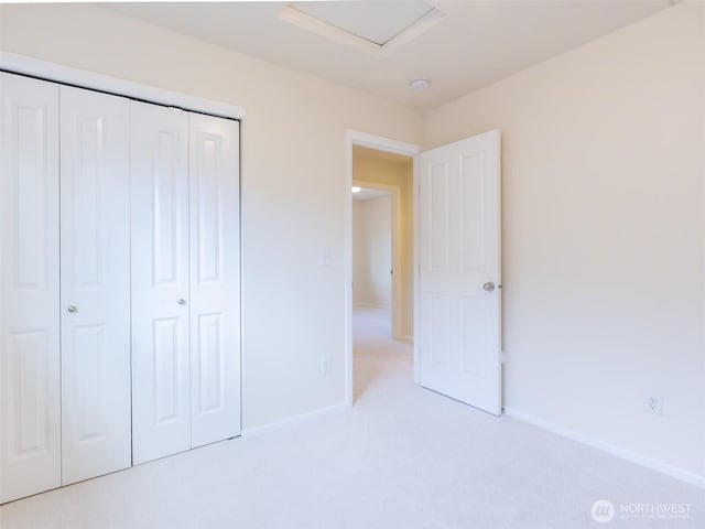 unfurnished bedroom with baseboards, carpet, a closet, and attic access