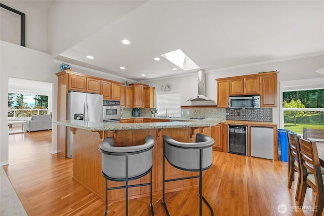 kitchen with appliances with stainless steel finishes, wall chimney exhaust hood, a wealth of natural light, wine cooler, and a skylight