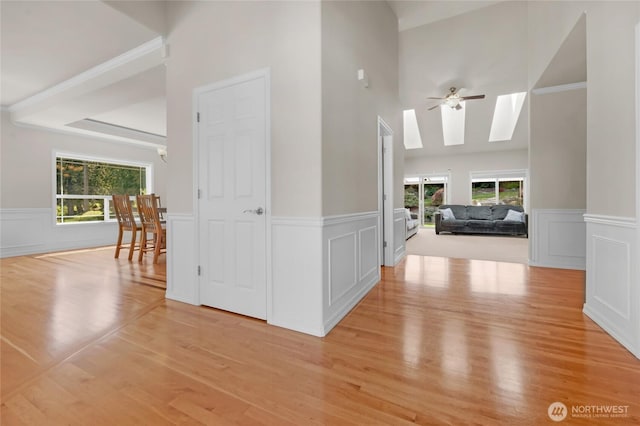 hallway featuring a skylight, wainscoting, a decorative wall, and light wood-style flooring