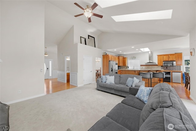 living area with high vaulted ceiling, light colored carpet, recessed lighting, a ceiling fan, and a skylight