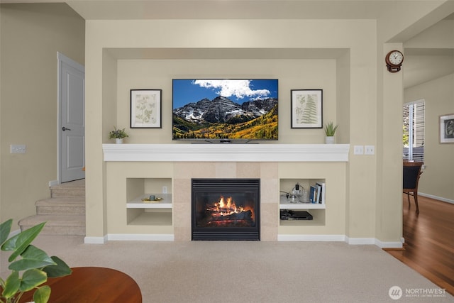 living area featuring baseboards, built in shelves, a tiled fireplace, and carpet flooring