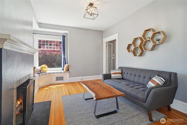 living area featuring a fireplace with flush hearth, wood finished floors, and baseboards