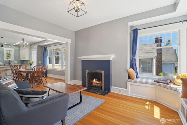 living room featuring a chandelier, light wood finished floors, a brick fireplace, and baseboards