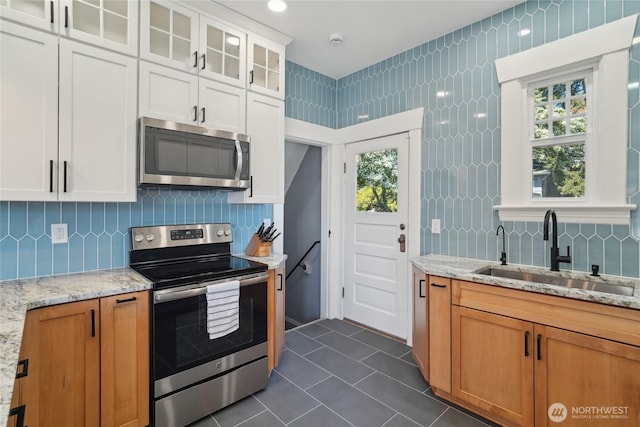 kitchen with stainless steel appliances, a sink, dark tile patterned floors, glass insert cabinets, and plenty of natural light