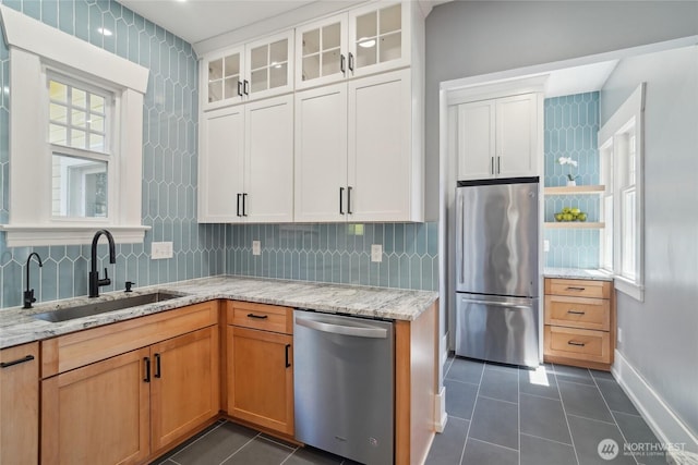 kitchen featuring appliances with stainless steel finishes, a sink, dark tile patterned flooring, light stone countertops, and decorative backsplash