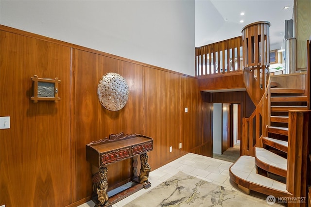 entryway featuring stairs, a towering ceiling, and wooden walls
