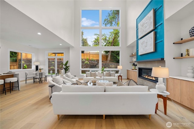 living room featuring recessed lighting, light wood-style floors, a tiled fireplace, and a towering ceiling
