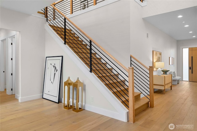 stairway featuring wood-type flooring, recessed lighting, baseboards, and a high ceiling