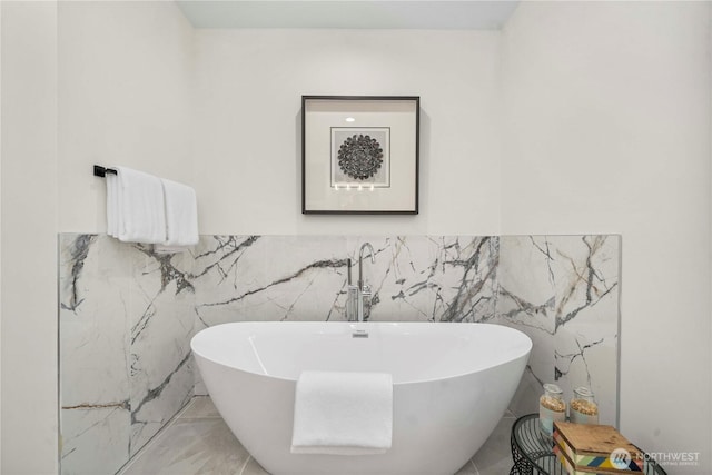 full bath with a freestanding bath, tile walls, and marble finish floor