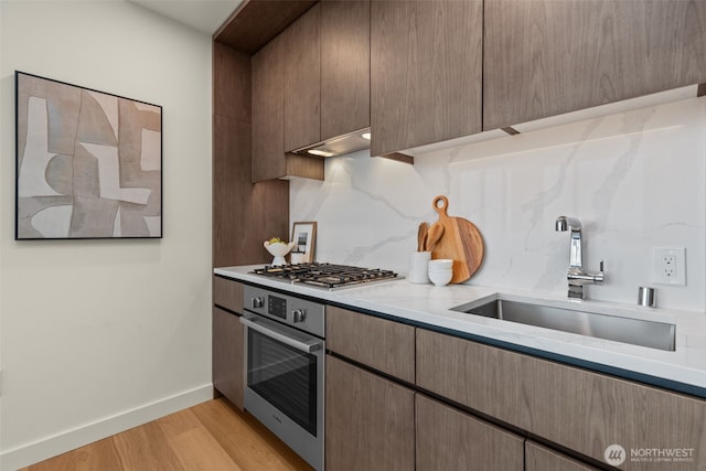 121 Stewart St Unit 2807, Seattle, WA 98101 - kitchen with appliances with stainless steel finishes, light wood-type flooring, decorative backsplash, light stone counters, and under cabinet range hood