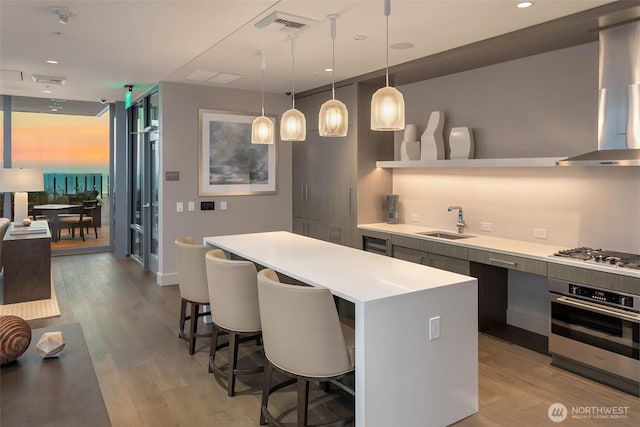 121 Stewart St Unit 2807, Seattle, WA 98101 - kitchen featuring stainless steel appliances, modern cabinets, a kitchen breakfast bar, wall chimney range hood, and light wood-style flooring