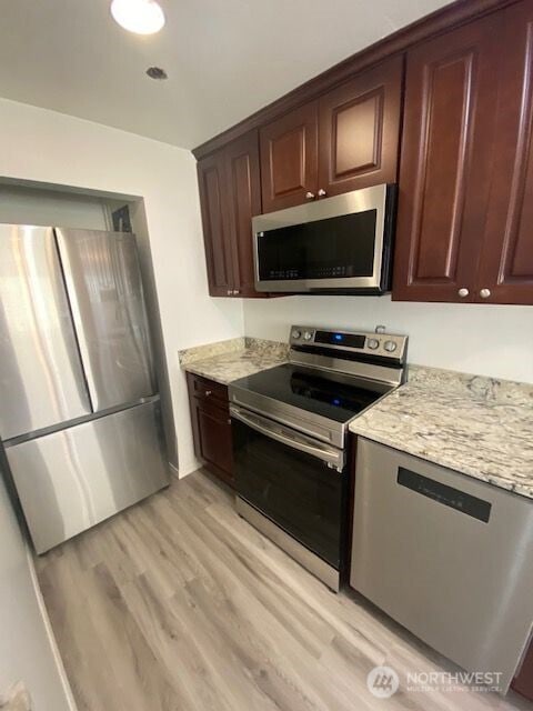 110 NW 39th St, Seattle, WA 98107 - kitchen with stainless steel appliances, light stone counters, light wood-style flooring, and dark brown cabinets