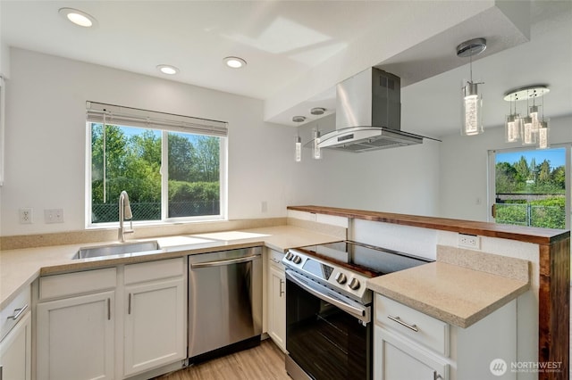 kitchen featuring appliances with stainless steel finishes, island range hood, a sink, a peninsula, and light countertops