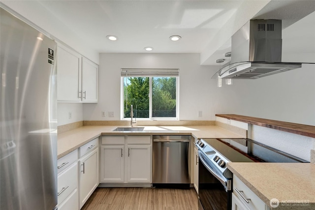 kitchen with stainless steel appliances, island exhaust hood, a sink, light wood finished floors, and white cabinets