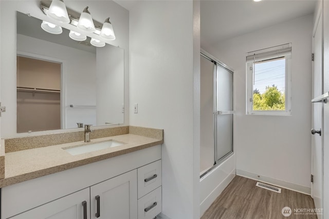 bathroom featuring wood finished floors, vanity, enclosed tub / shower combo, baseboards, and a spacious closet