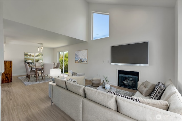 living area with light wood finished floors, a glass covered fireplace, baseboards, and a high ceiling