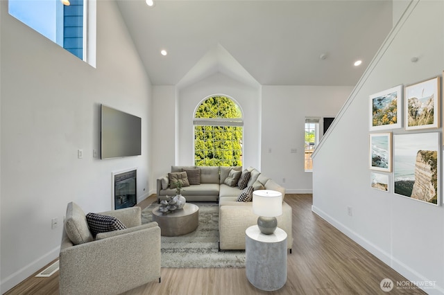 living room featuring vaulted ceiling, baseboards, wood finished floors, a glass covered fireplace, and recessed lighting