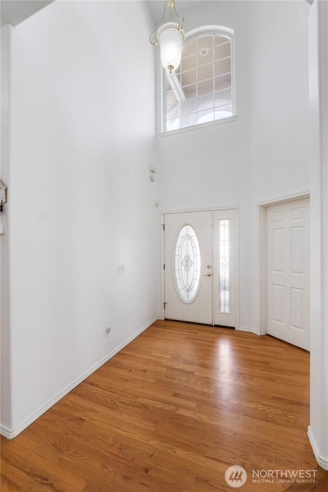entryway with baseboards, a notable chandelier, a high ceiling, and wood finished floors
