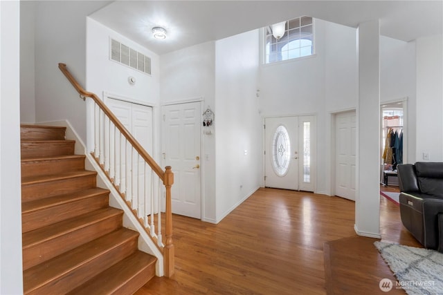 entryway with stairway, visible vents, a high ceiling, and light wood-style floors