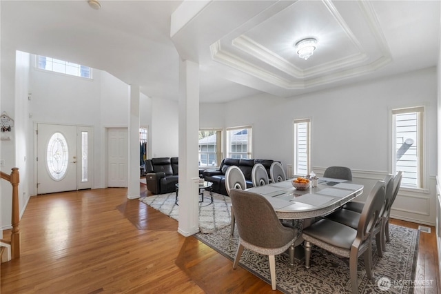 dining room with a tray ceiling, crown molding, and light wood-style flooring