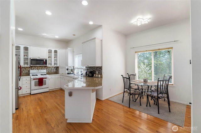 kitchen featuring appliances with stainless steel finishes, glass insert cabinets, a peninsula, decorative backsplash, and light wood-type flooring